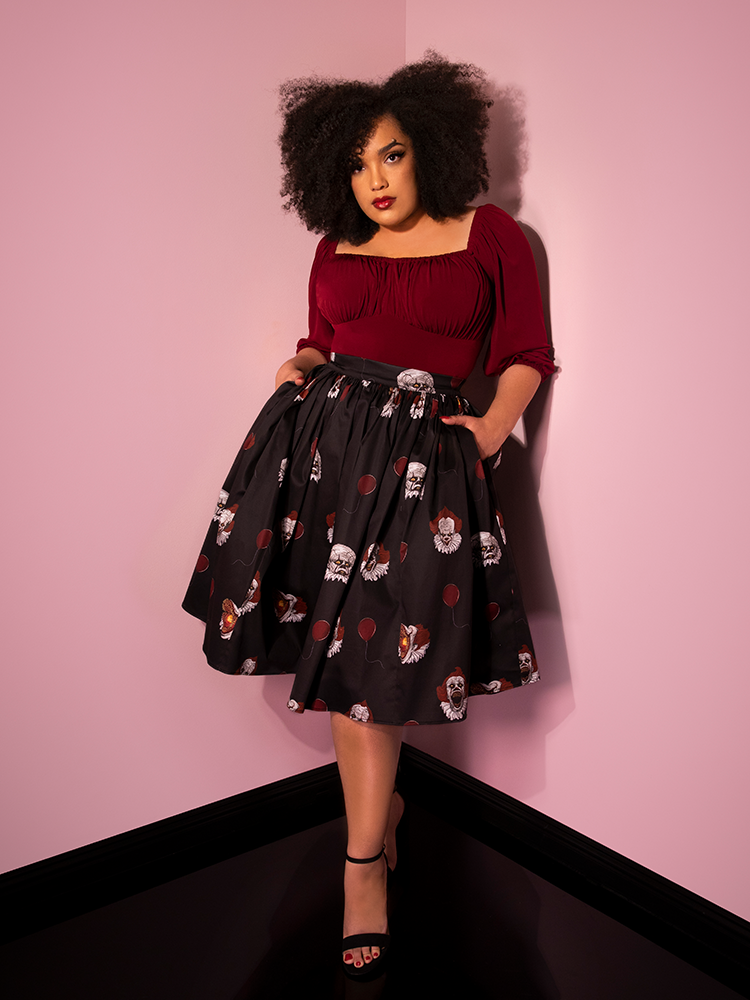 Looking at the camera with her hands in her pockets, Ashleeta shows off her Pennywise swing skirt in black by Vixen Clothing.