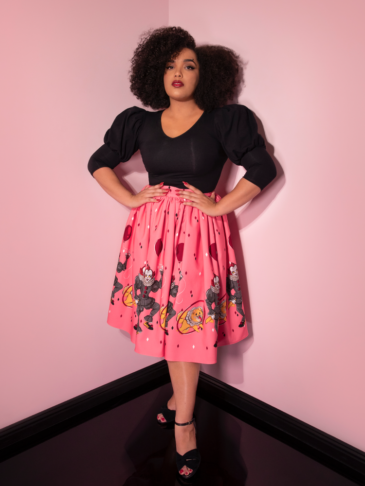 Looking at the camera with her hands on her hips, Ashleeta showcases the Pennywise dancing clown swing skirt in pink by Vixen Clothing.