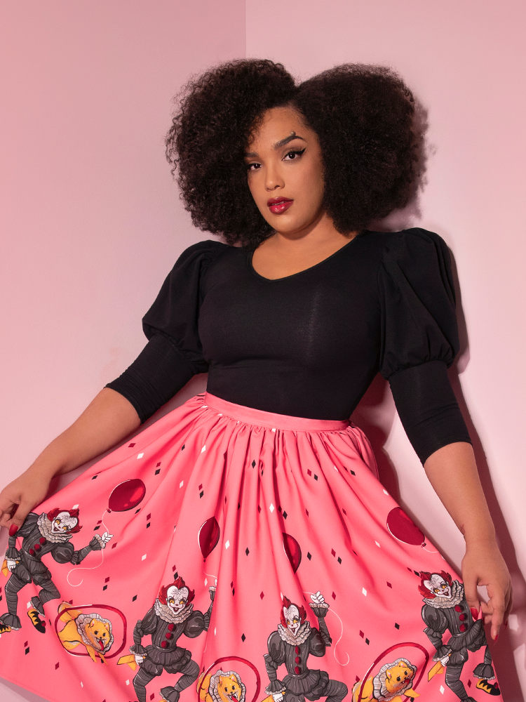 Looking at the camera while holding her skirt, Ashleeta models the Carnival top in black by Vixen Clothing.