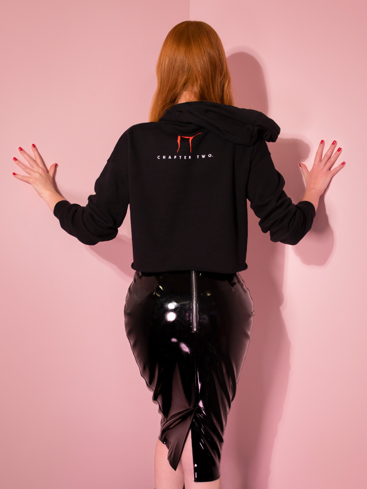 Turned away from the camera with her hands against a pink wall, Emily models the Home At Last cropped hoodie by Vixen Clothing.