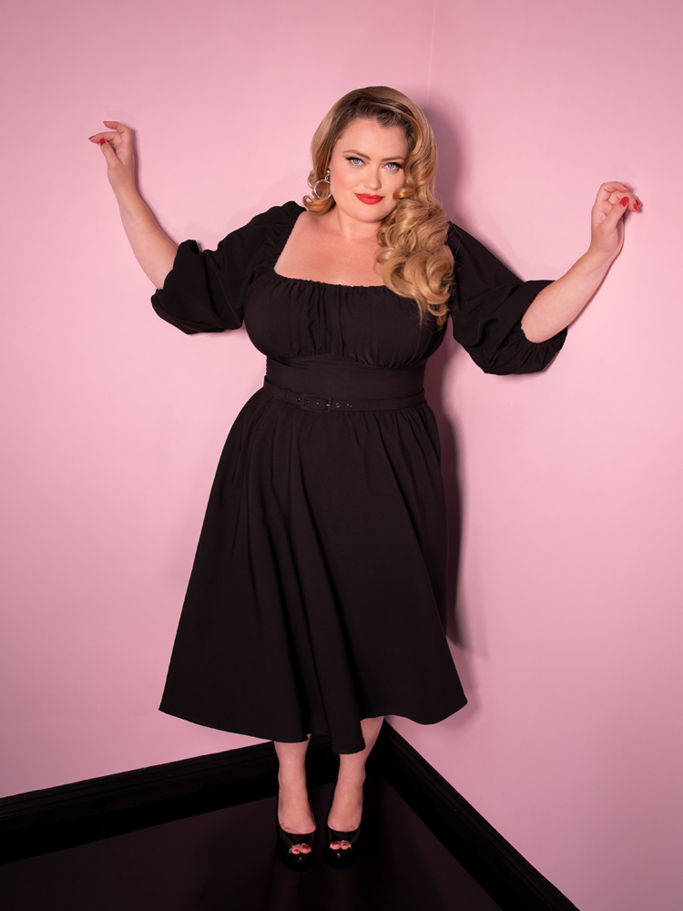 Blondie with her arms raised shows off the Vacation Dress in Black from retro clothing brand Vixen Clothing.