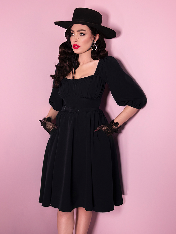 Micheline Pitt wearing a retro era dress in black with matching hat and lace gloves. 