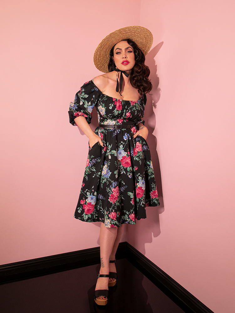 Full length shot of Micheline Pitt wearing a floral retro style dress and sunhat.