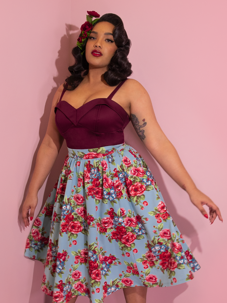 A closeup of Ashleeta wearing flowers in her hair and a wine colored top modeling the Vacation skirt in blue and red rose print.