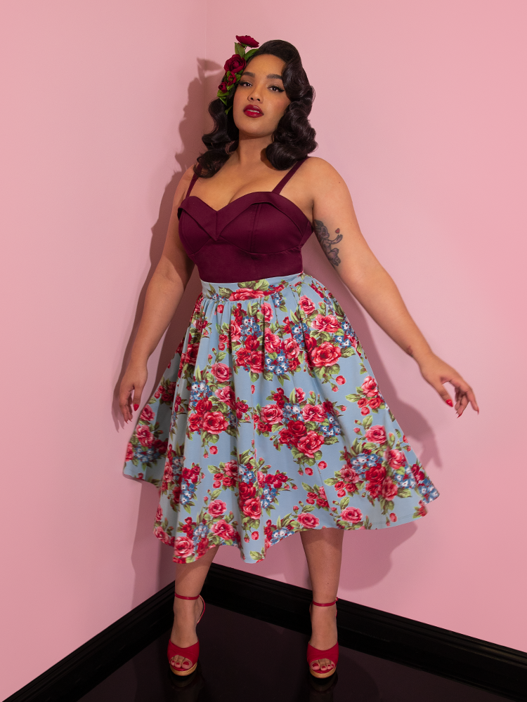 Ashleeta wearing flowers in her hair and a wine colored top modeling the Vacation skirt in blue and red rose print.