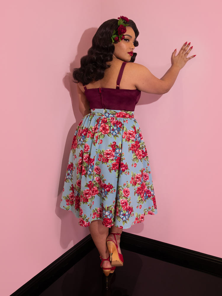 Ashleeta looking over her shoulder wearing flowers in her hair and a wine colored top modeling the Vacation skirt in blue and red rose print.