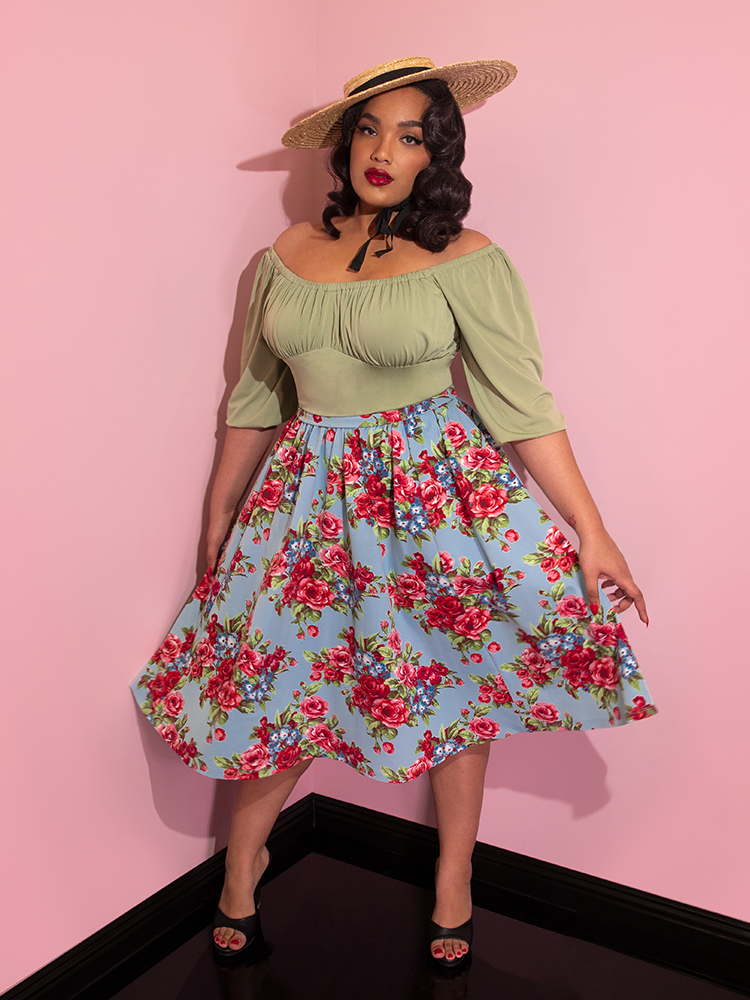 Ashleeta wearing a straw hat and green top modeling the Vacation skirt in blue and red rose print.