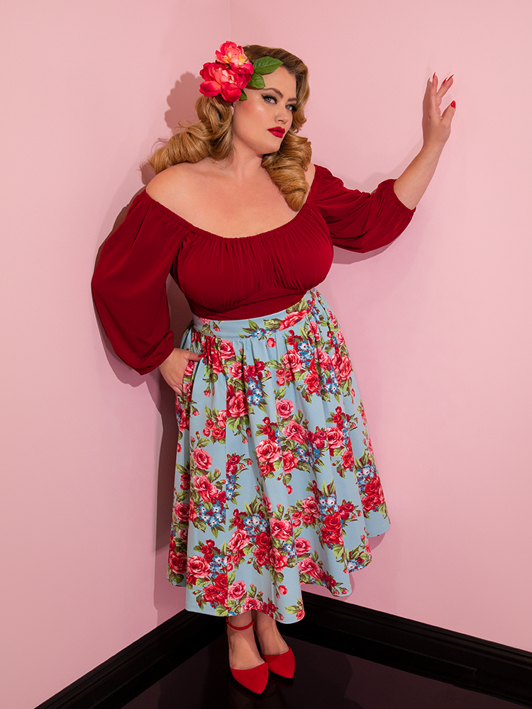 Blondie wearing flowers in her hair and a red top modeling the Vacation skirt in blue and red rose print.