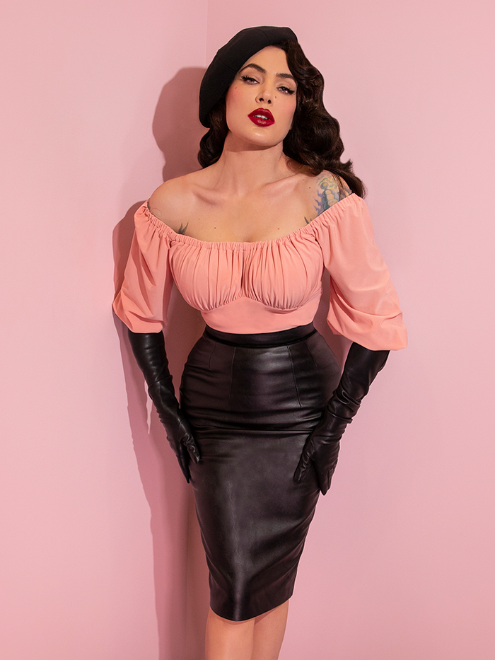 A closeup of Micheline Pitt wearing a black beret, pink top, and elbow length gloves modeling the Vixen pencil skirt in vegan leather.