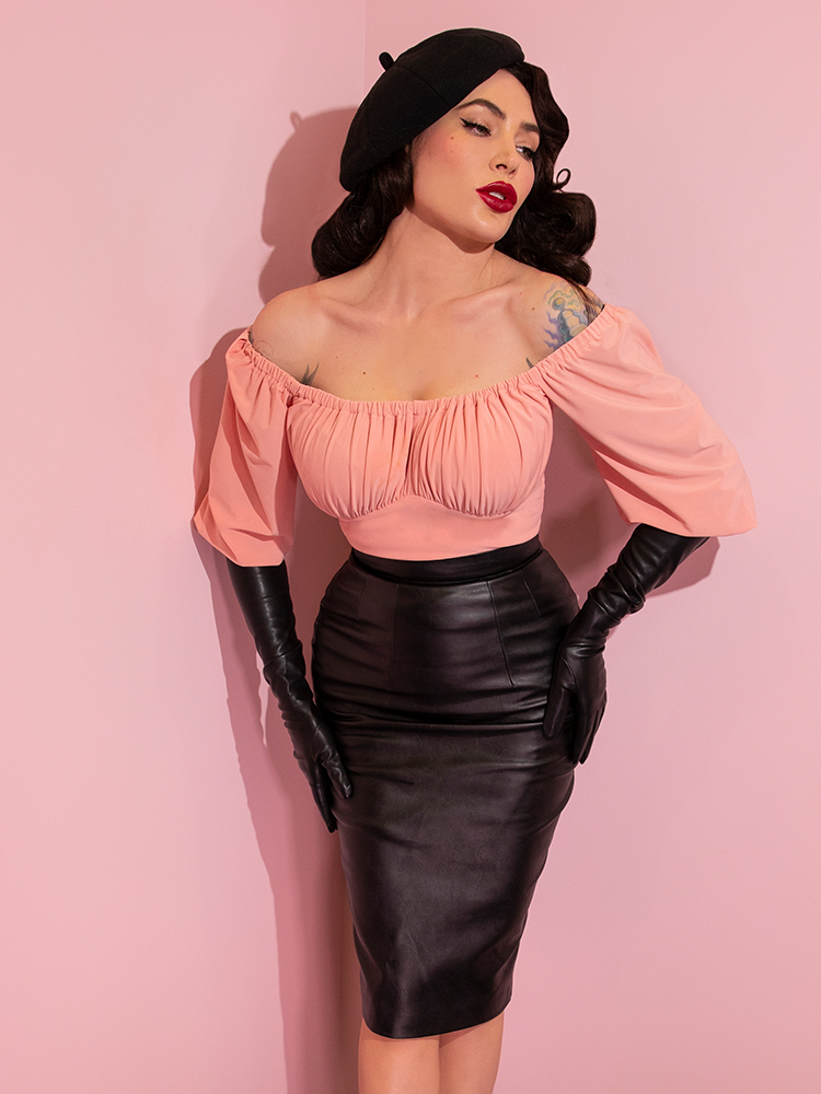 A closeup of Micheline Pitt looking away from camera modeling the Vacation top in pink paired with black gloves and a black skirt.