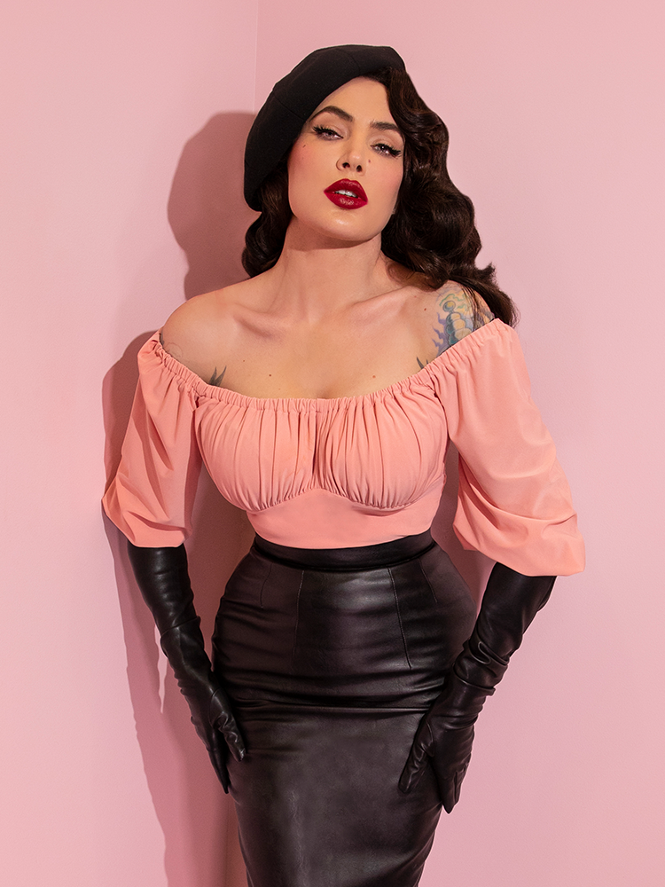 A closeup of Micheline Pitt looking at the camera modeling the Vacation top in pink paired with black gloves and a black skirt.