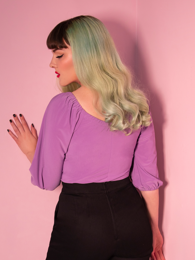 Back shot of model in a lavender vacation blouse and black high waisted pants.