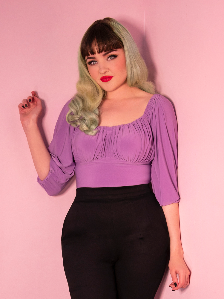 Posing model wearing black high waisted retro era pants and a lavender top.