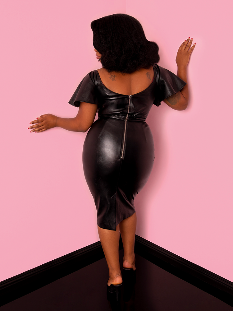 A back view of Aretina wearing a black flutter sleeve top modeling the Vixen pencil skirt in vegan leather.