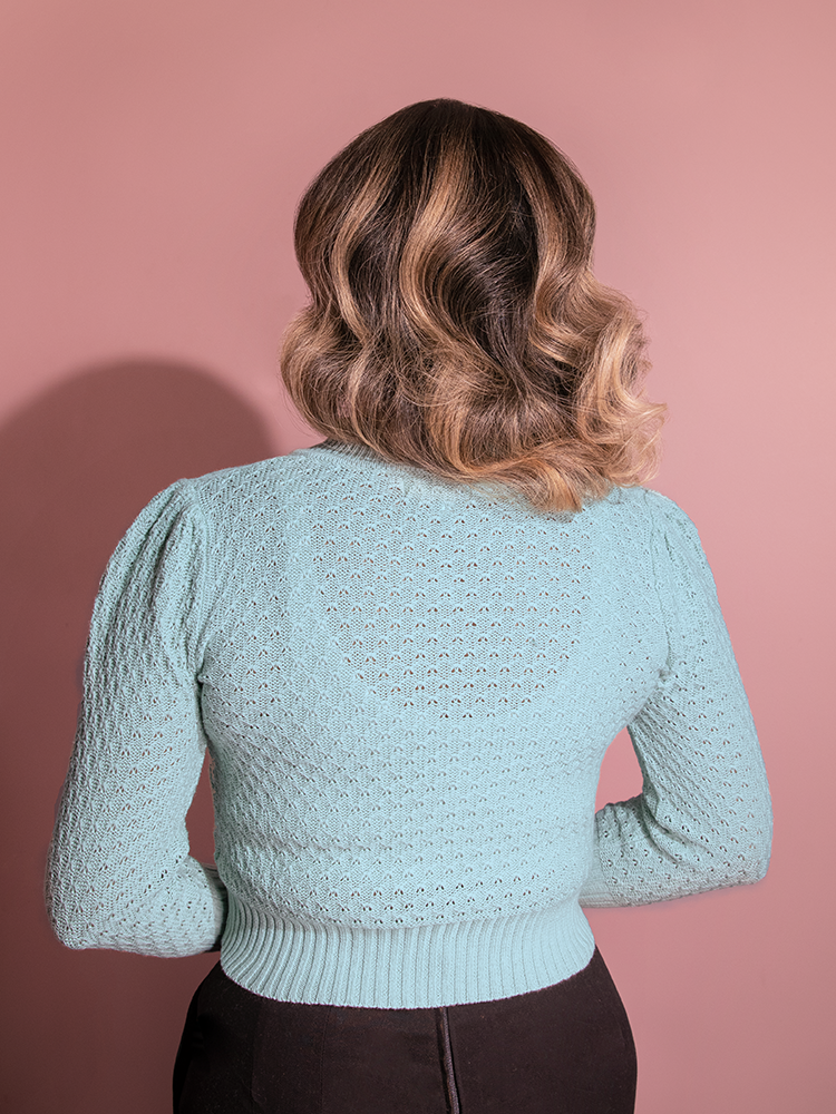 Gaby elegantly shows off the back of the all-new Vintage-Style Cropped Crew Neck Knit Cardigan in Light Blue from Vixen Clothing in her pose.