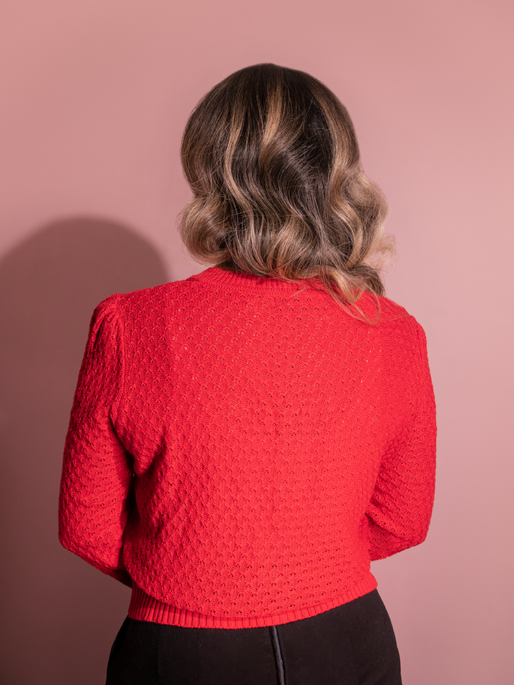 Gaby looks away from the camera while posing in the Vintage-Style Cropped Crew Neck Knit Cardigan in Red from Vixen Clothing during her modeling shoot.