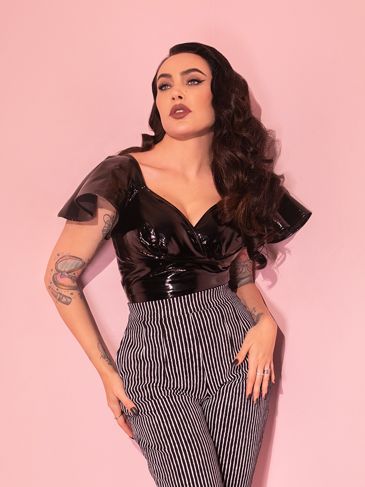 Micheline Pitt looking upwards and posing in the Miss Kitty Babydoll Top in Black Vinyl from Vixen Clothing.
