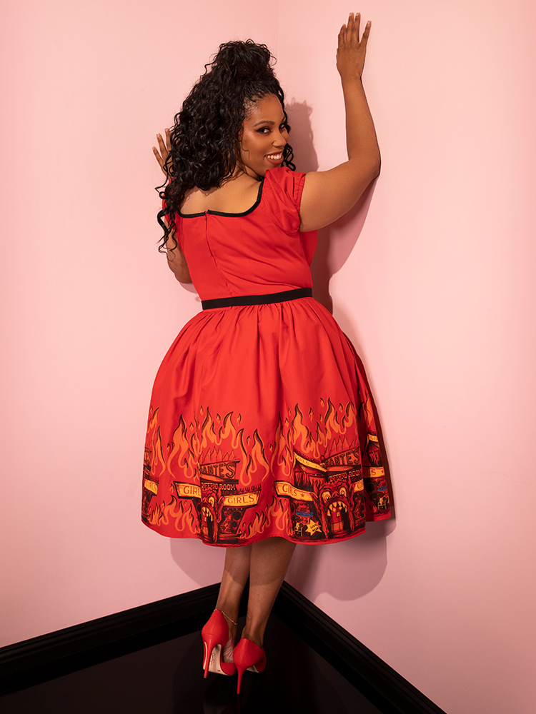 Model turned away from the camera to give a glimpse of the back of the BEETLEJUICE™ Dante's Inferno Swing Dress from Vixen Clothing.