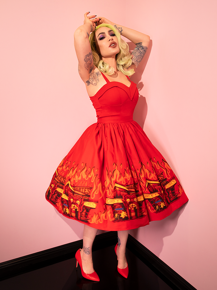 Micheline Pitt posing with his arms up over her head posing in an all red outfit including the BEETLEJUICE™ Dante's Inferno Swing Skirt and low-cut red retro top.