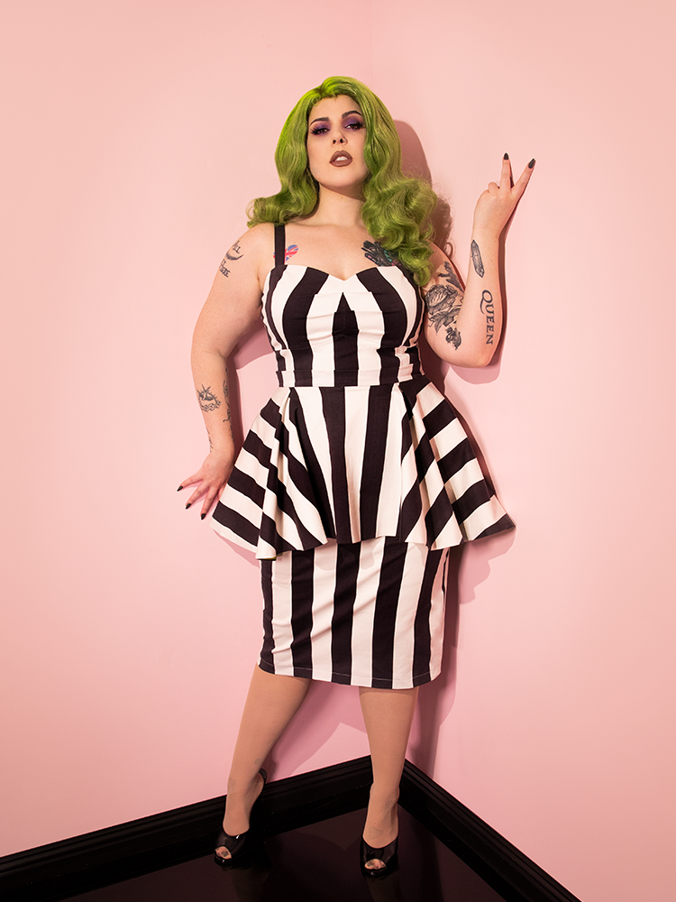 Green haired female model wearing the BEETLEJUICE™ Ghost with the Most Peplum Dress from retro dress company Vixen Clothing.