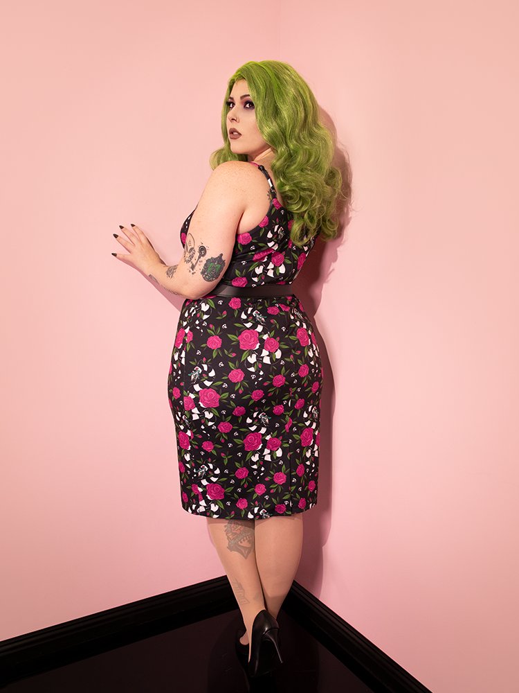 Green haired female model facing away from the camera to show off the back of the BEETLEJUICE™ Sandworm & Roses Peplum Wiggle Dress.'