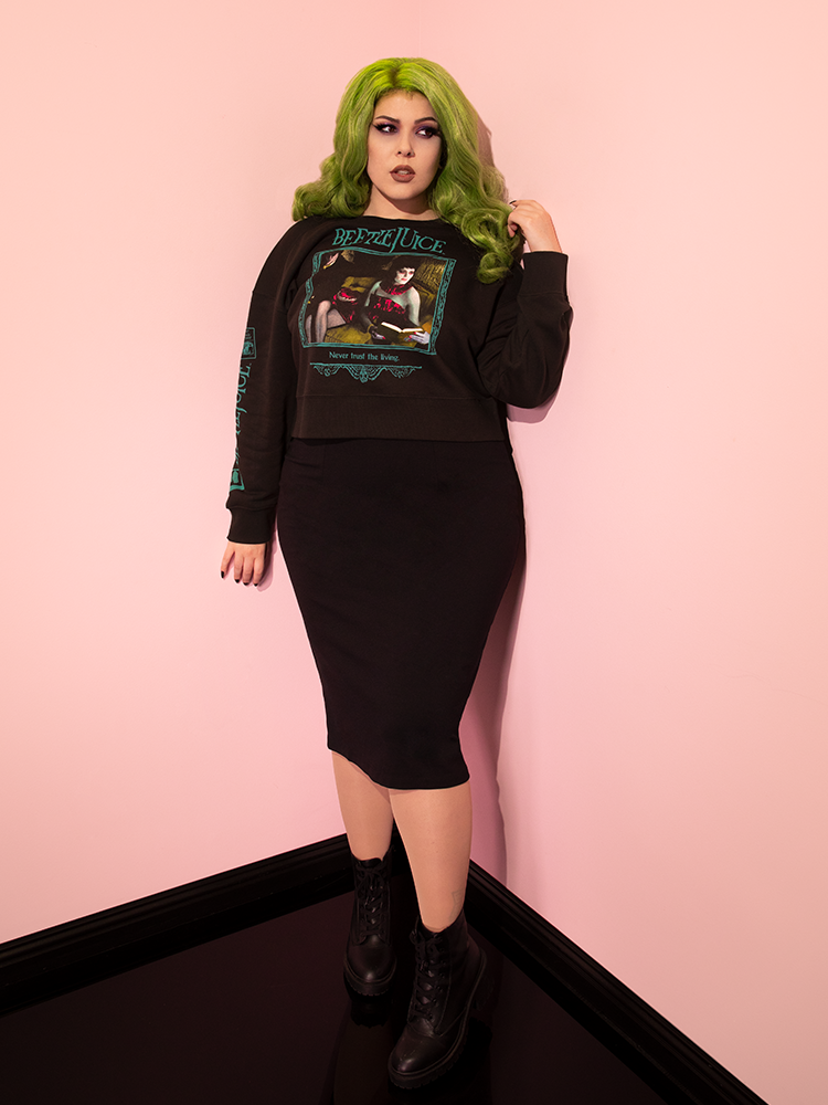 Full length shot of green haired female model wearing the Waiting Room Sweatshirt with black retro skirt and ankle-length combat boots.
