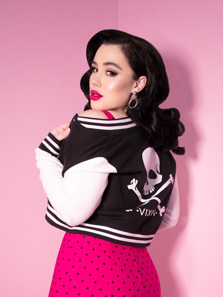 Rachel Sedory facing away from the camera with her Vixen Girl Gang Letterman Jacket hanging off of her shoulder while wearing a hot pink retro skirt with black polka dots.