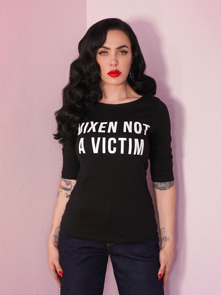 A closeup photo of Micheline Pitt looking off camera modeling the Vixen Not A Victim t-shirt untucked by Vixen Clothing.