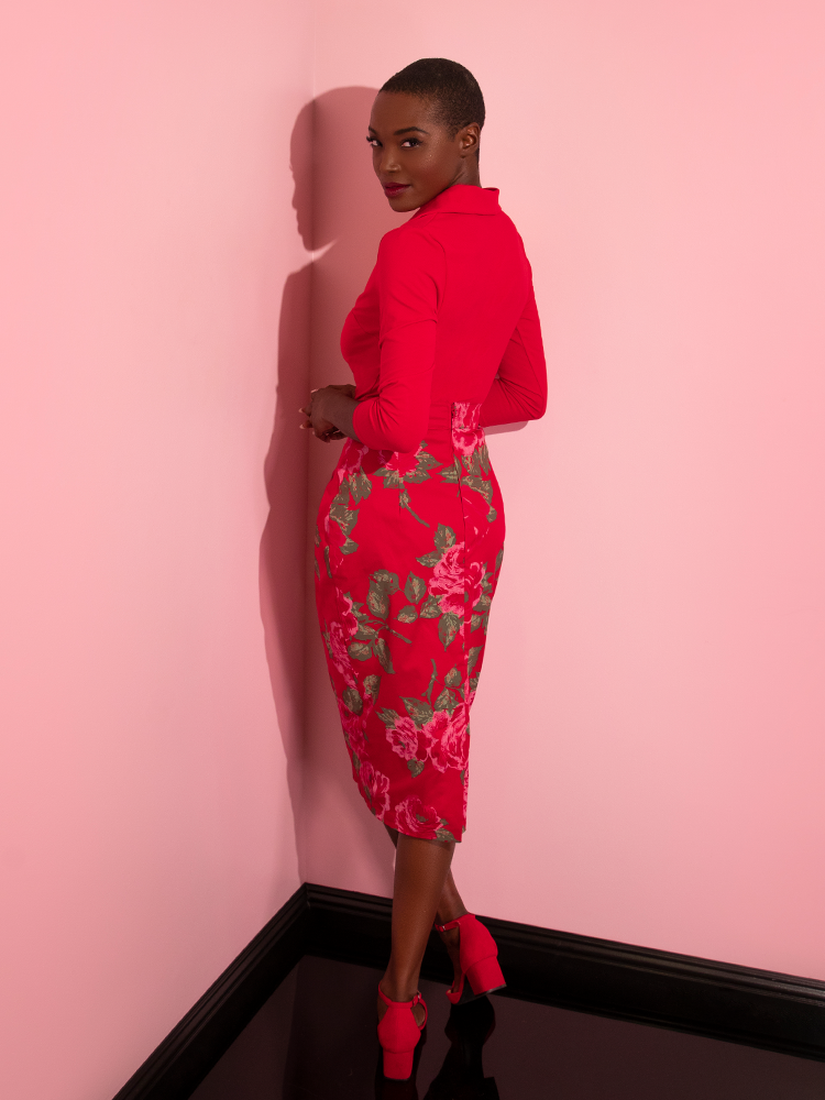 Brittany facing away from the camera turns back to look at it, giving the viewer a glimpse of the back of the Vixen Pencil Skirt in Vintage Red Rose Print.