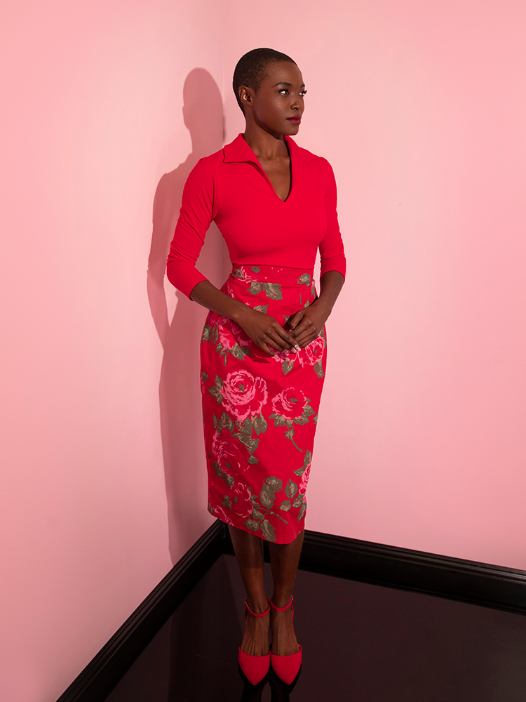 Brittany looks off camera while her clasping her hands gently at her midsection while modeling the Vixen Pencil Skirt in Vintage Red Rose Print.