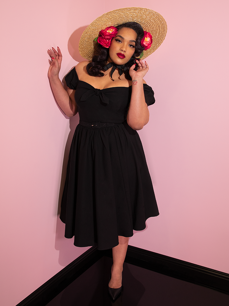 Ashleeta wearing a straw hat and flowers in her hair modeling the Vixen dress in black.