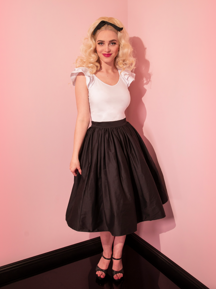 Full length shot of blonde model smiling and looking at the camera while wearing the Vixen Swing Skirt in Black from retro clothing brand Vixen Clothing.