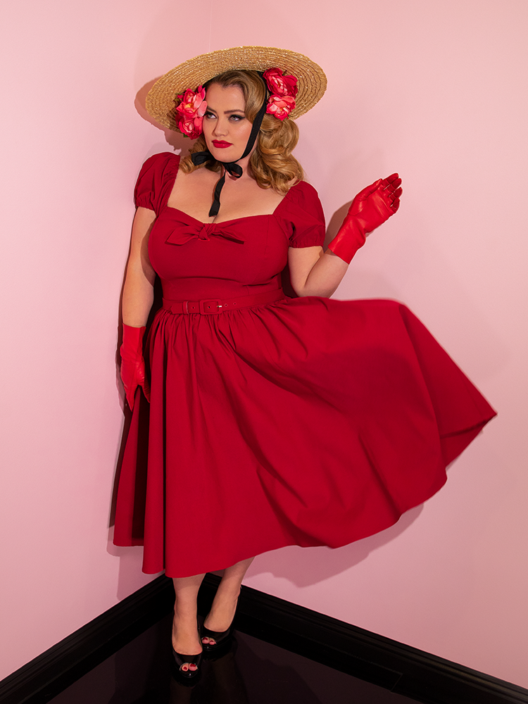 Full length shot of Blondie in a red retro dress paired with a natural colored sunhat.