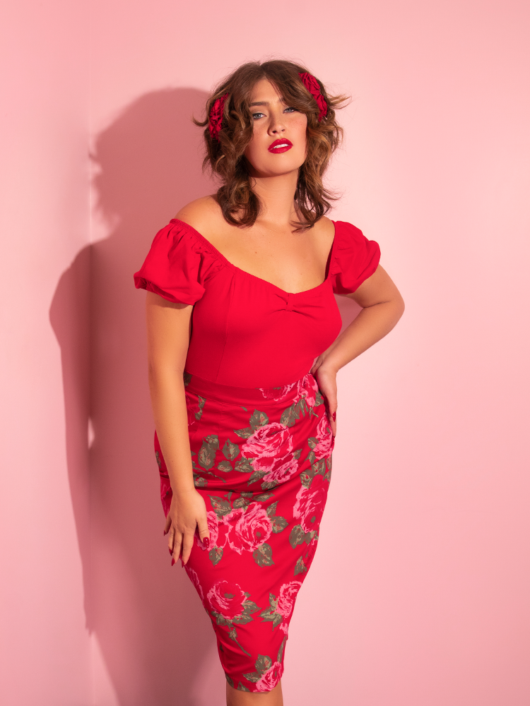Francesca with one hand on her hip, gazes into the camera while wearing an all red outfit including the all-new Vixen Pencil Skirt in Vintage Red Rose Print from Vixen Clothing.