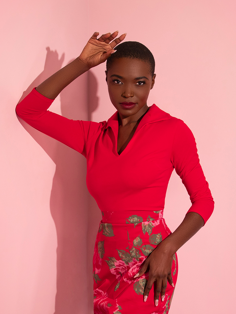 Female model posing while wearing the Vixen Top in Ravishing Red  with matching pink rose retro skirt.