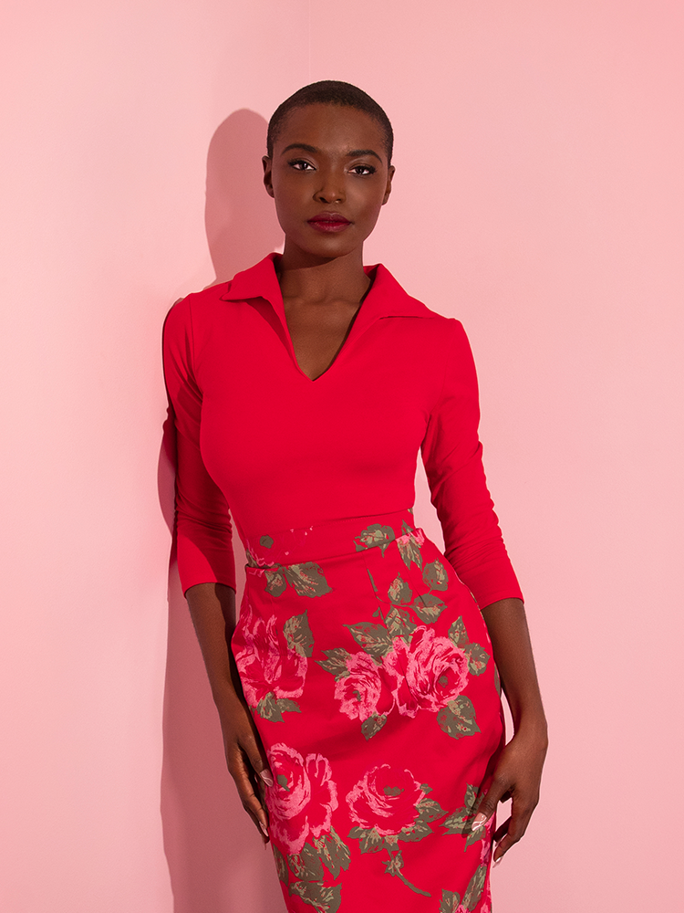 Photographed from the knees up, a female model wears the Vixen Top in Ravishing Red with a complimentary pink rose skirt.
