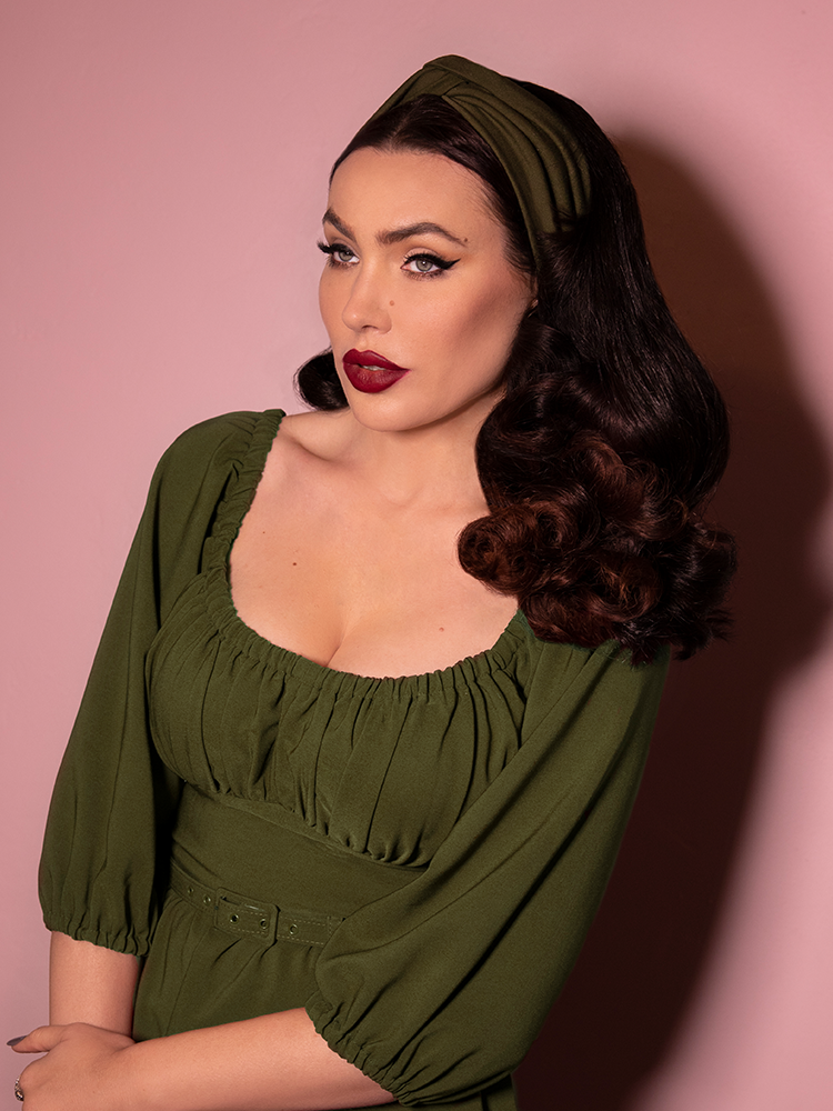 Looking past the camera, Micheline Pitt models the vintage style knot headband in olive green paired with a matching dress.