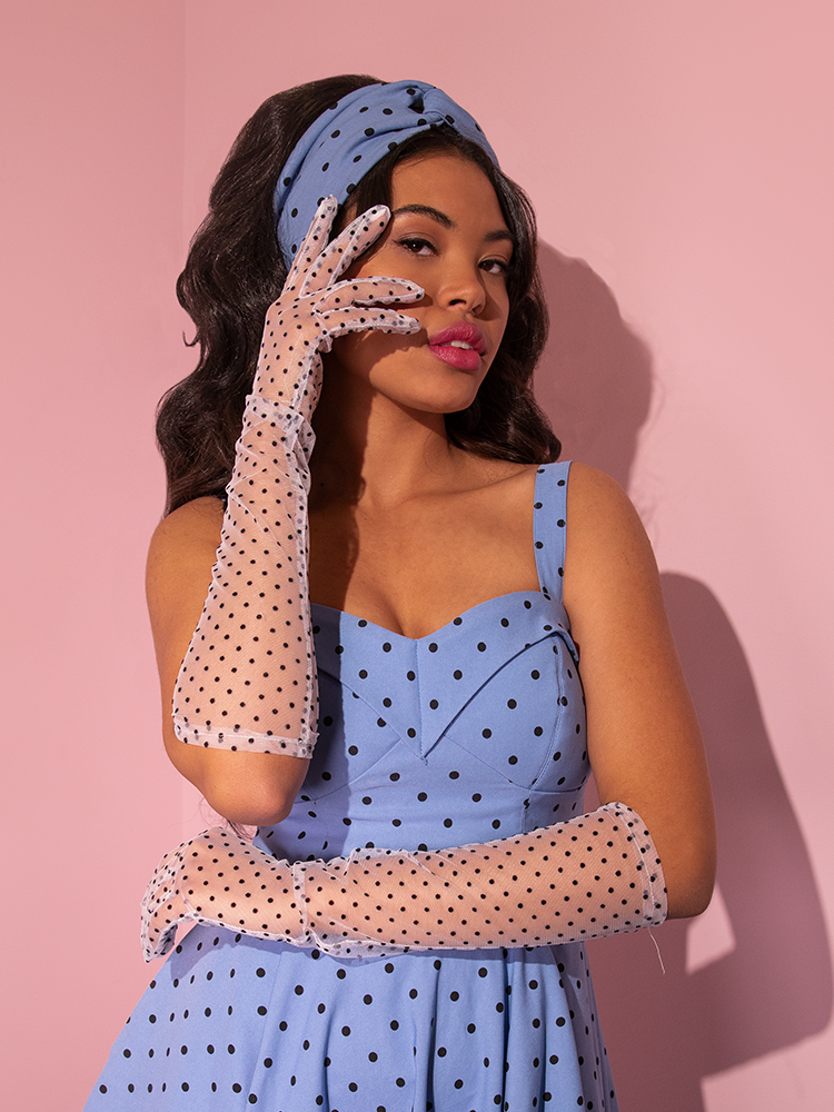 The Mesh Polka Dot Mid Length Gloves in White being modeled by a model in a corn-blue retro inspired dress from Vixen Clothing.