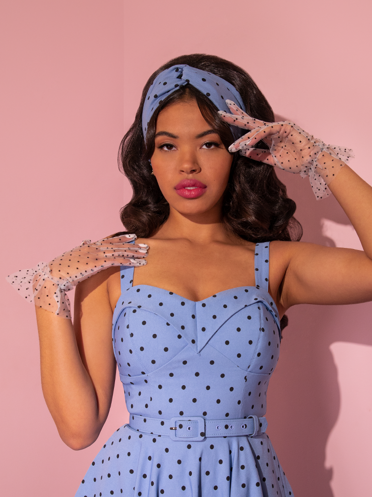 Shot from the waist up, a model poses with the Mesh Polka Dot Gloves in White and corn blue retro style dress.