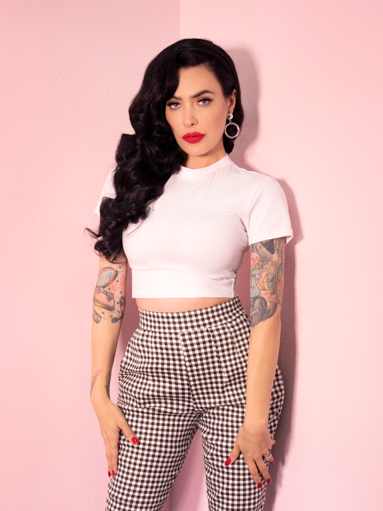 A closeup of Micheline Pitt looking at the camera modeling the Bad Girl crop top in white paired with gingham cigarette pants.