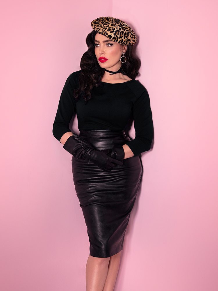 A closeup of Micheline Pitt wearing a leopard beret, black top, and black gloves modeling the Vixen pencil skirt in vegan leather.