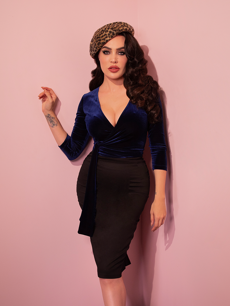Micheline Pitt from Vixen Clothing looks effortlessly stylish in the Wrap Top in Midnight Blue Velvet and black retro skirt, available now from the retro fashion brand.