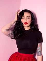 A closeup of Micheline Pitt with her hand in her hair modeling the Bad Girl crop top in black by Vixen Clothing.