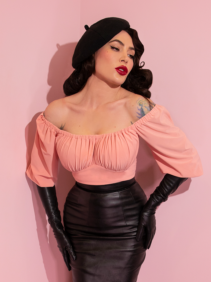 A closeup of Micheline Pitt looking away from camera modeling the Vacation top in pink paired with black gloves and a black skirt.