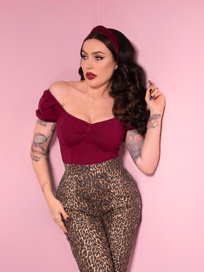 Micheline Pitt wearing the Powder Puff Top in Burgundy paired with leopard print cigarette pants and a burgundy headband. All retro clothing items available from Vixen Clothing!