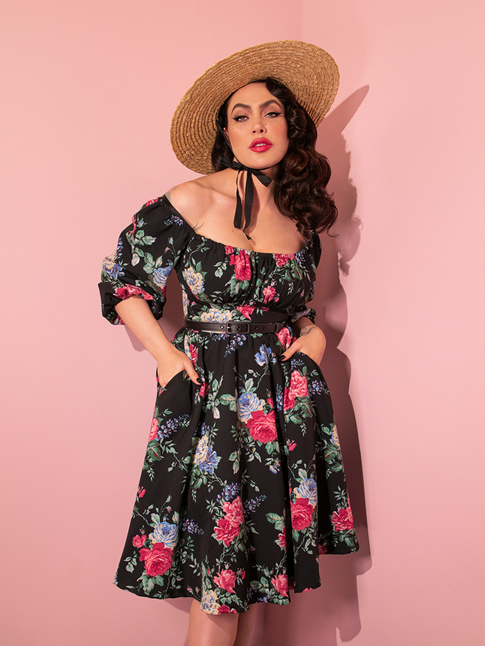 Micheline Pitt tucks her hand into the pockets of the Vacation Dress in Black Rose Print. 