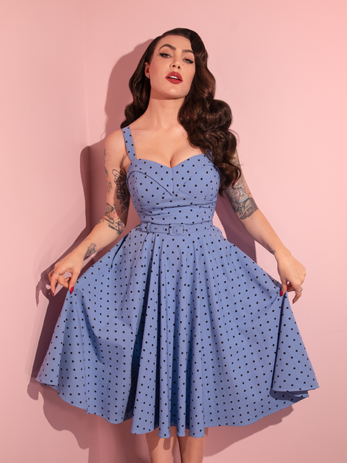 Micheline Pitt holds the sides of the skirt on the Maneater Swing Dress in Sunset Blue Polka Dot.