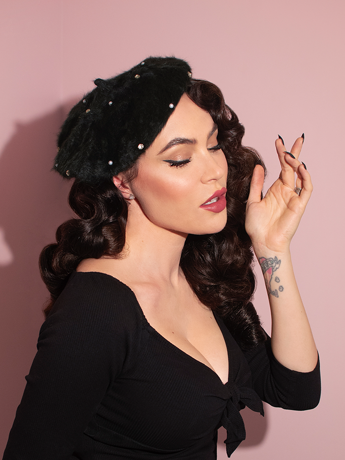 Profile shot of Micheline Pitt wearing the Vintage Style Beret with Rhinestones in Black to complement her black retro top.
