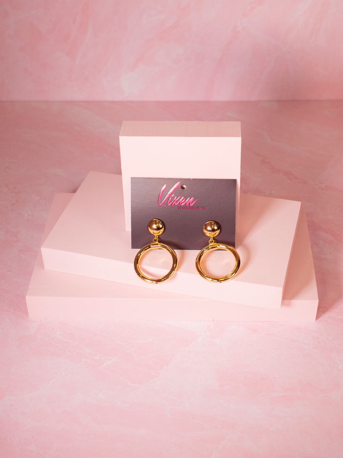 Gold hoop earrings photographed on a pink layout - items available from retro clothing brand Vixen Cloting.