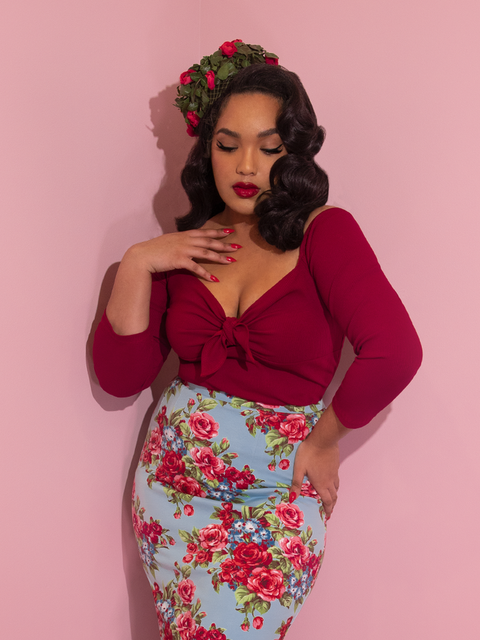 A closeup of Ashleeta modeling the tie me up top in red by Vixen Clothing paired with a blue floral skirt and floral pillbox hat.